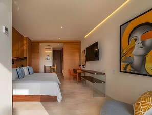 Ein modernes Hotelzimmer mit einem Bett, einem Schreibtisch und einem Sessel. Ein Fernseher ist an der Wand befestigt und über dem Schreibtisch hängt ein Gemälde.
