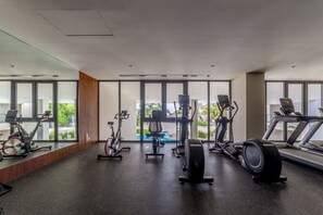 Ein Fitnessstudio mit verschiedenen Trainingsgeräten, großen Fenstern und Blick auf Grünflächen.
