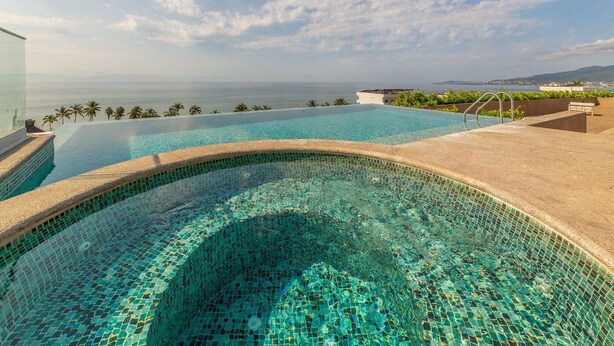 En infinitypool med mosaikmönstrade plattor, en klarblå himmel och utsikt över havet.