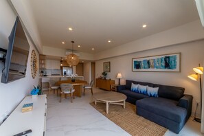 A modern living room with a dark blue sofa, a round coffee table, and a dining area with a wooden table and chairs. - Bucerias Ocean View 1 bdr new condo (Bucerías)