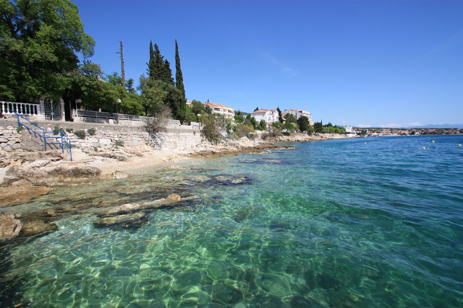 Una zona costera con aguas cristalinas, costa rocosa y edificios a lo largo de la línea de costa.