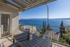 Ein Balkon mit Tisch, Stühlen und einer Weinflasche, mit Blick auf eine schöne Aussicht auf das Meer und die Berge.