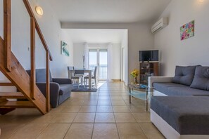 Ein geräumiger Wohnbereich mit Treppe, einem Esstisch mit Stühlen, einer Couch, einem Fernseher und einem Bücherregal.