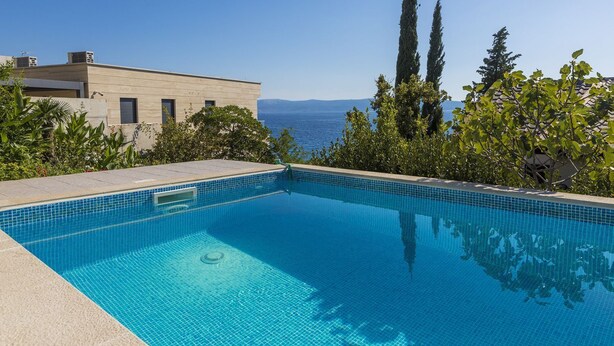 Ein rechteckiger Swimmingpool mit klarem, blauem Wasser, umgeben von einer gefliesten Terrasse.