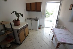 A compact kitchen with a sink, stove, and cabinets, a dining table with a tablecloth, and a potted plant. - Dog-friendly studio apartment just 80 metres from the beach with pool (Crikvenica)