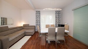 A modern living room with a sectional sofa, a dining table with chairs, a flat-screen TV, and a large window with curtains. - Idyllic apartment with pool, table tennis, summer kitchen, private parking (Crikvenica)