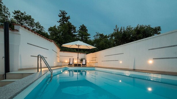 A swimming pool with steps leading into it, surrounded by white walls and a tiled roof. There are lounge chairs and an umbrella near the pool. - Idyllic apartment with pool, table tennis, summer kitchen, private parking (Crikvenica)