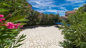 A courtyard with a stone floor, surrounded by greenery and a blue tennis table. - Idyllic apartment with pool, table tennis, summer kitchen, private parking (Crikvenica)