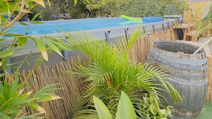 Area piscina con recinto in bambù, una grande botte e diverse piante tropicali.