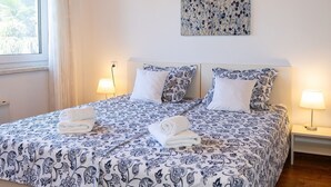 Un lit bien fait, recouvert d’une couvre-lit à motifs floraux et agrémenté d’oreillers, deux lampes de chevet et une fenêtre avec des rideaux.
