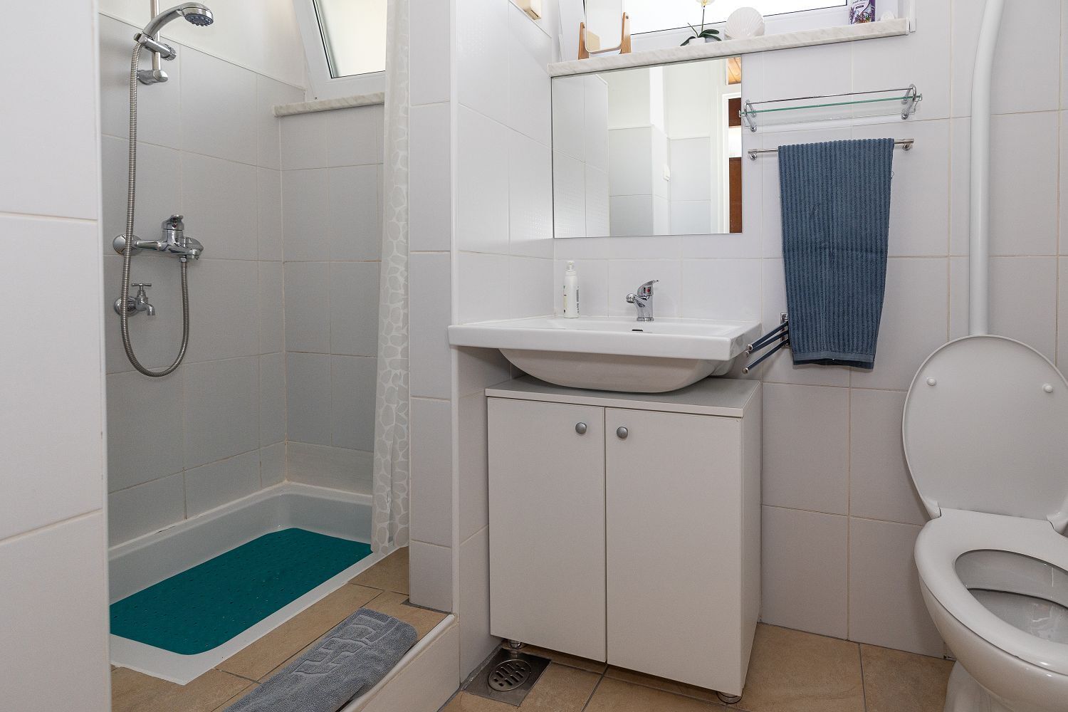 A bathroom with a shower, sink, toilet, and a mirror above the sink.