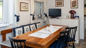 Une pièce chaleureuse avec une table à manger en bois, des chaises bleues, un téléviseur et des coussins sur le thème de la marine.