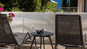 Une terrasse avec deux fauteuils et une table, offrant une vue panoramique sur la mer et les collines.