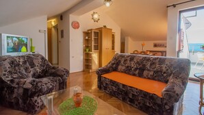 Ein Wohnzimmer mit zwei gemusterten Sofas, einem Glastisch, einem Fernseher, einer Uhr und einem Bücherregal.