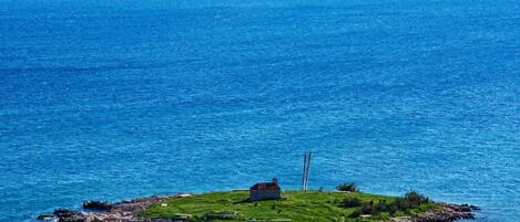 A small island with a single building surrounded by rocky shores and clear blue water.