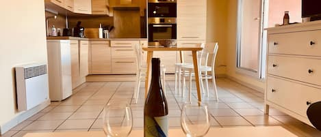 Eine moderne Küche mit Essbereich, mit einem Tisch, Weingläsern und einer Flasche, einem eingebauten Ofen und einem großen Fenster.