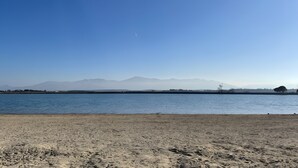 En strand med klar himmel, roligt vand og fjerne bjerge.