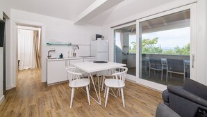 Una cocina moderna con armarios blancos, un comedor con mesa y sillas blancas, y un balcón con vistas al exterior.
