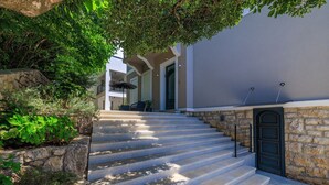 Una escalera de piedra que conduce a la entrada de un edificio, rodeada de vegetación y un muro de piedra.
