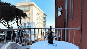 A balcony with a table set for two, a bottle of wine, and two wine glasses. - Cozy Flat by the Beach (Jesolo)