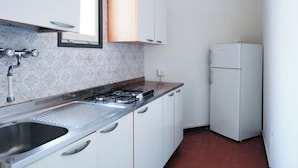 A kitchen with white cabinets, a gas stove, a sink, and a white refrigerator. - Cozy Flat by the Beach (Jesolo)