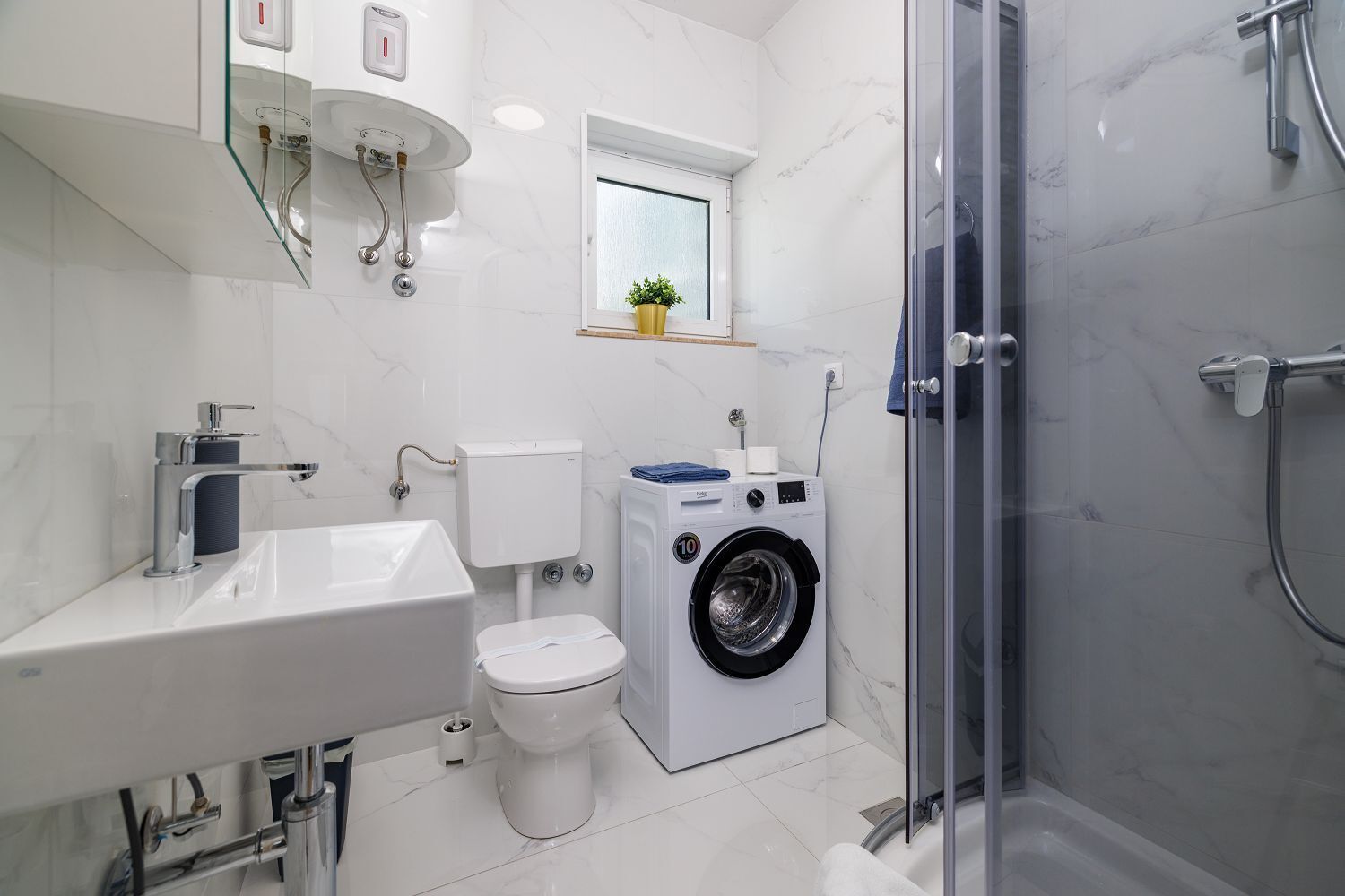 A modern bathroom with a sink, toilet, washing machine, and shower.