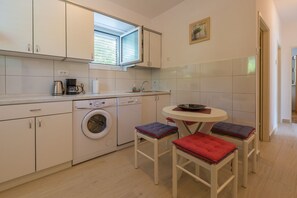 A compact kitchen with a washing machine, a coffee maker, and a small dining table with chairs. - Large apartment just 300 metres from the beach with sea views and washing machine (Dramalj)