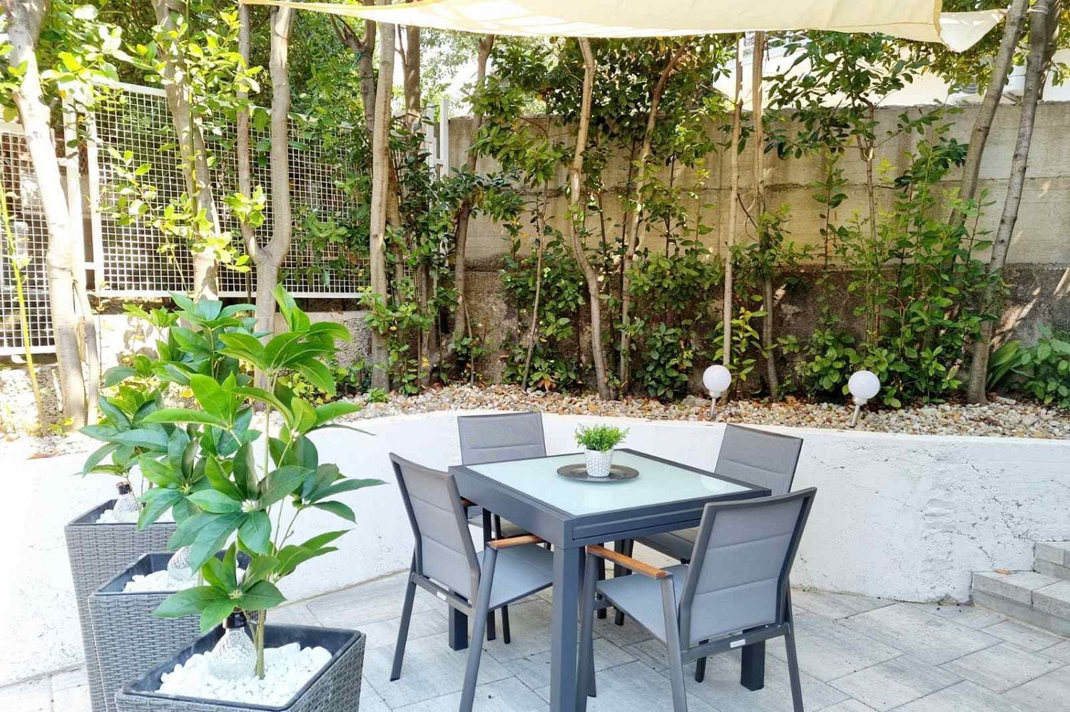 Patio esterno con tavolo e sedie, immerso nel verde e delimitato da una recinzione.