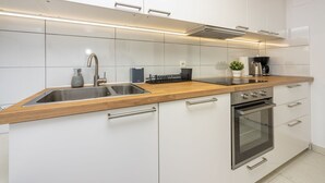 Moderni keittiö, jossa on valkoiset kaapit, ruostumattomasta teräksestä valmistetut kodinkoneet, puinen työtaso ja sisäänrakennettu uuni.
