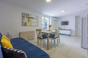 Ein modernes Wohnzimmer mit einem blauen Sofa, einem Esstisch mit Stühlen, einem Gemälde an der Wand und einem Fernseher über einem weißen Schrank.