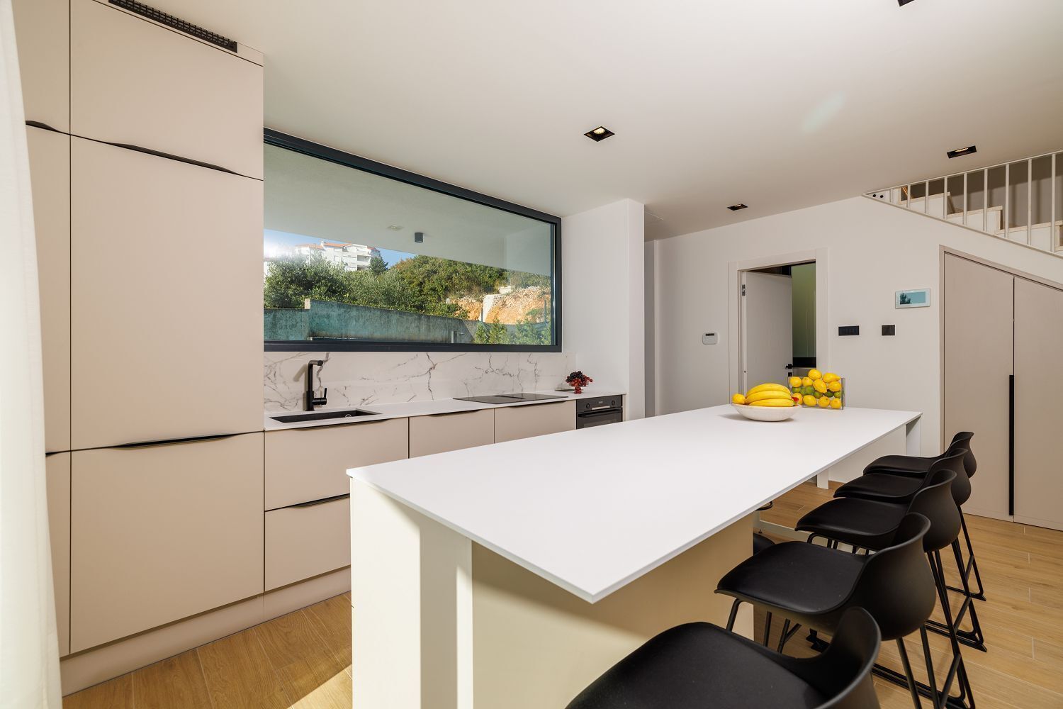 Une cuisine moderne dotée d’une grande fenêtre, de meubles blancs et d’un îlot central avec des chaises noires.