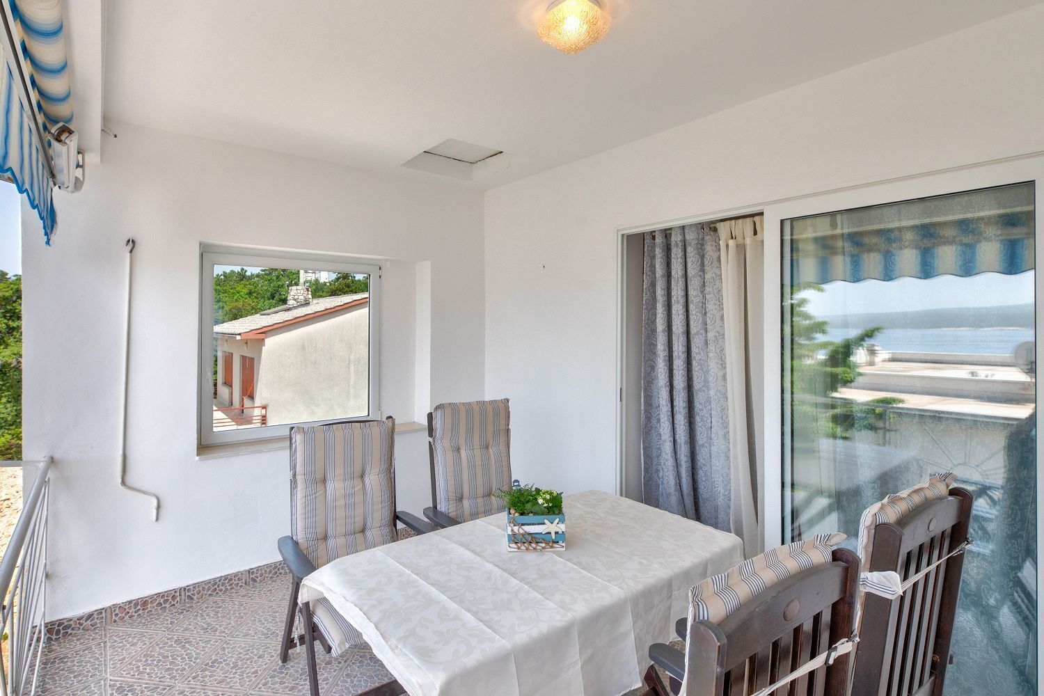 Un balcon avec une table et des chaises, une vue sur la mer et une fenêtre donnant sur un immeuble.