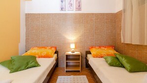 Ein kleiner, gemütlicher Raum mit zwei Betten, jedes mit grünen und orangefarbenen Kissen, einem Nachttisch mit Lampe und einer Wand mit Backsteinmusterfliesen.