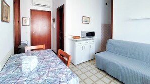 A compact living space with a dining table, a sofa, a microwave, and a small kitchenette. - Comfy Flat With Pool and Balcony (Jesolo)