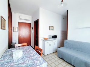 A compact living space with a dining table, a sofa, a microwave, and a small kitchenette. - Comfy Flat With Pool and Balcony (Jesolo)
