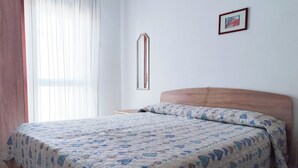 A bedroom with a bed, a wooden headboard, a bedside table, a mirror, and a framed picture on the wall. - Comfy Flat With Pool and Balcony (Jesolo)