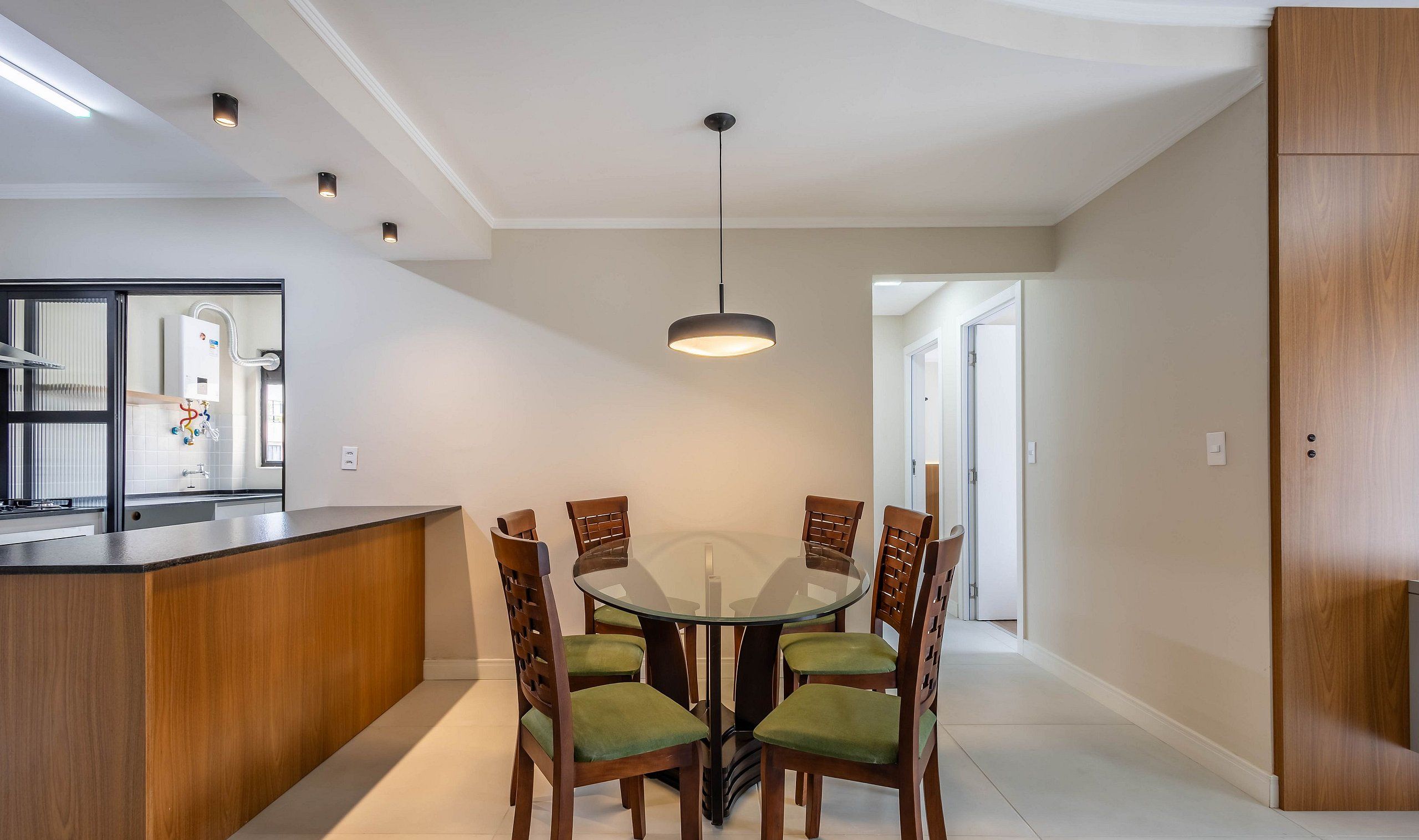 A modern kitchen with a central island, a dining area with a round glass table and wooden chairs, and a pendant light above.