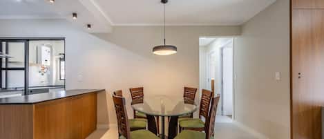 A modern kitchen with a central island, a dining area with a round glass table and wooden chairs, and a pendant light above.