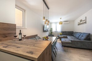 A modern living space with a wooden dining table, a grey sofa, and a kitchen area with a wine bottle and glass. - Completely renovated apartment just 500 metres from the beach with barbecue, smart TV and tumble dryer (Crikvenica)