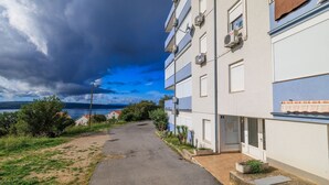 Ein schmaler Pfad führt zu einem mehrstöckigen Gebäude mit Klimaanlagen, einem kleinen Eingang und Blick aufs Meer.
