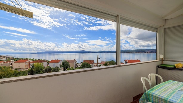 Ein Balkon mit Tisch und Stühlen, mit Blick auf einen See und Gebäude in der Ferne.