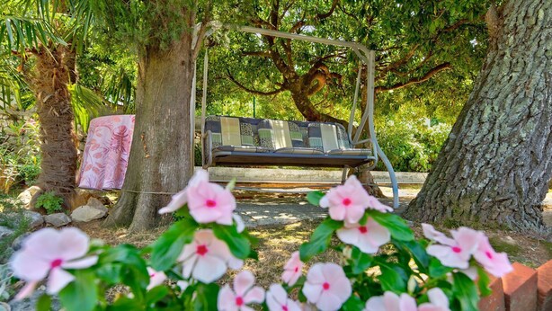 Um jardim com cadeira de balanço, um banco e flores cor-de-rosa em primeiro plano.