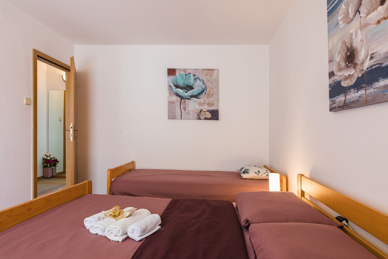 A room with two beds, a wooden headboard, a painting on the wall, and a door leading to another room.