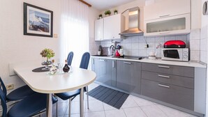 Uma cozinha moderna com armários cinza, bancada branca, micro-ondas vermelho e um espaço de refeições com duas cadeiras e uma mesa.
