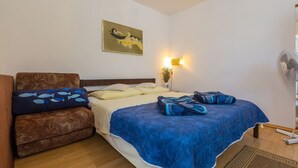 Une chambre à coucher comprenant un lit, un canapé, une lampe fixée au mur, un ventilateur et un tableau.