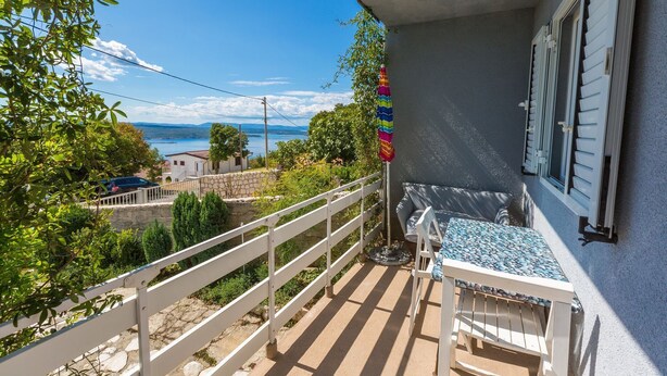 Un balcon avec vue sur la mer, une balustrade blanche et une table avec des chaises.