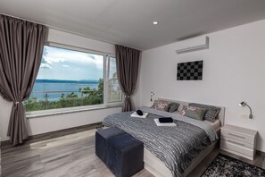 Ein modernes Schlafzimmer mit einem großen Bett, Meerblick und einem Wandbild mit Schachmuster.