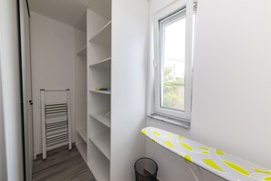 Ein schmaler Flur mit weißen Wänden, einem Heizkörper und einem Fenster mit Blick auf Grün.