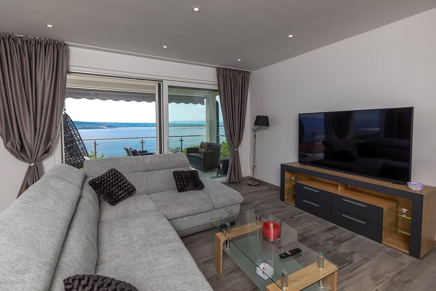 A modern living room with a grey sofa, a flat-screen TV, and a glass coffee table.