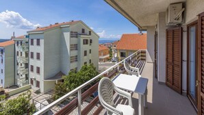 Un balcon avec une table et des chaises, donnant sur une ville côtière aux bâtiments aux toits de tuiles rouges.